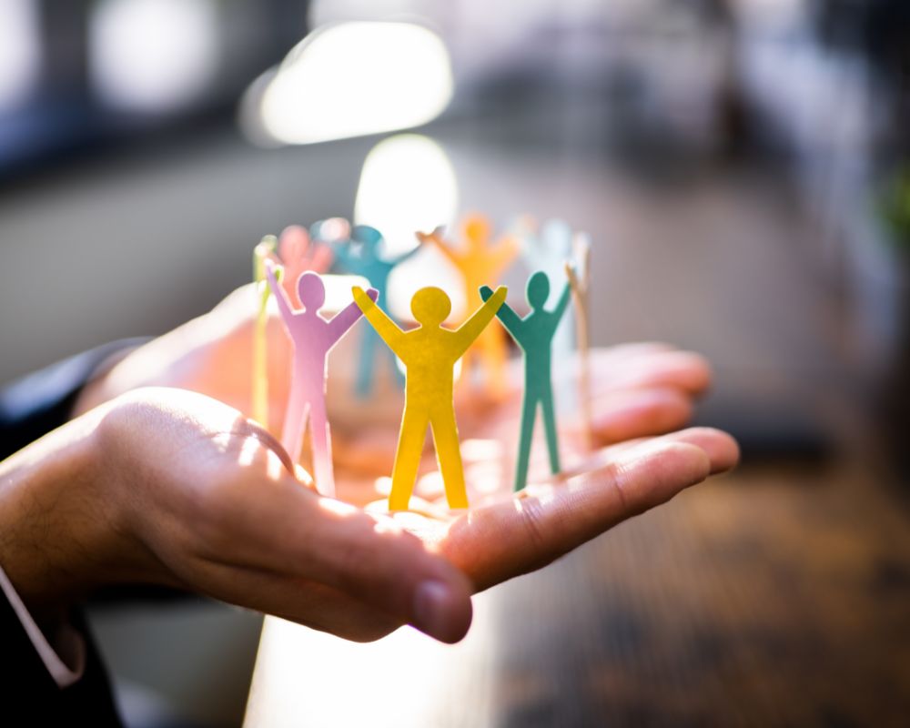 Manos sosteniendo figuras de papel en círculo representando comunidad y trabajo en equipo